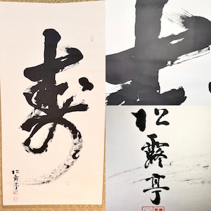 May include: A vertical scroll featuring bold black ink calligraphy on a white background. The artwork displays large, expressive brushstrokes forming characters, with smaller text and red seal stamps visible in the lower left corner.