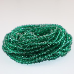 Peut inclure: Un brin enroulé de perles à facettes vert émeraude. Les perles sont petites et réfléchissent la lumière, créant un effet scintillant. Le mot "Neerem" est imprimé sur les perles. Les perles sont probablement destinées à la fabrication de bijoux ou à l'artisanat.