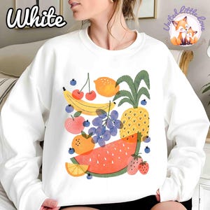 May include: White sweatshirt featuring a colorful fruit illustration. The design includes a banana, cherries, lemon, apple, grapes, pineapple, watermelon, and strawberries. The word "White" is printed in the upper left corner.