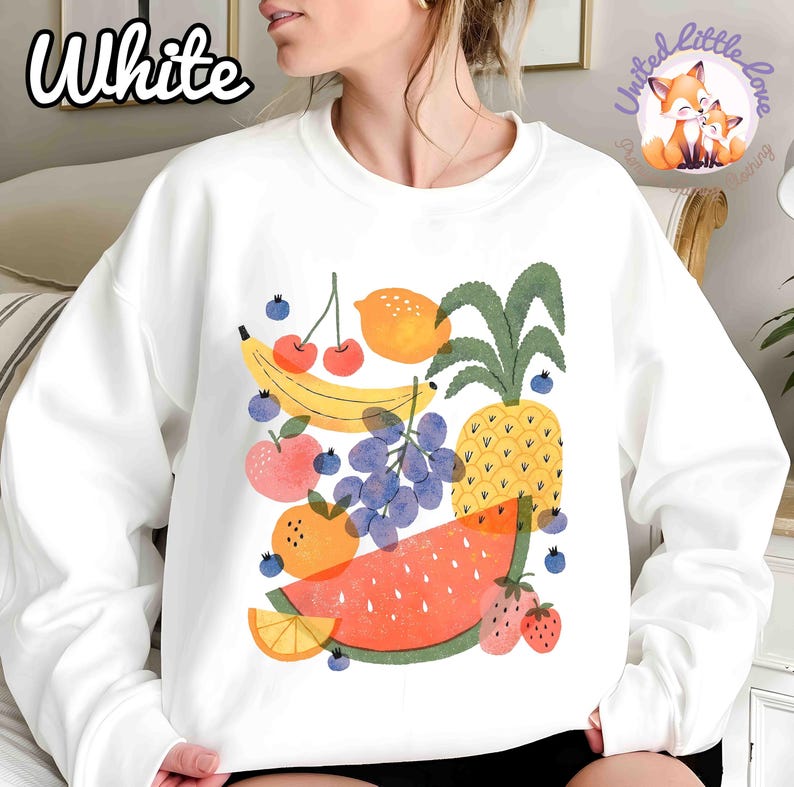 May include: White sweatshirt featuring a colorful fruit illustration. The design includes a banana, cherries, lemon, apple, grapes, pineapple, watermelon, and strawberries. The word "White" is printed in the upper left corner.