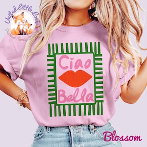 K&ouml;nnte beinhalten: Hellrosa Sweatshirt mit einem Aufdruck, der "Ciao Bella" in Rosa und Orange zeigt, mit einem orangefarbenen Lippen-Design. Das Design ist von gr&uuml;nen Streifen umrahmt. Das Sweatshirt hat einen Rundhalsausschnitt und lange &Auml;rmel.