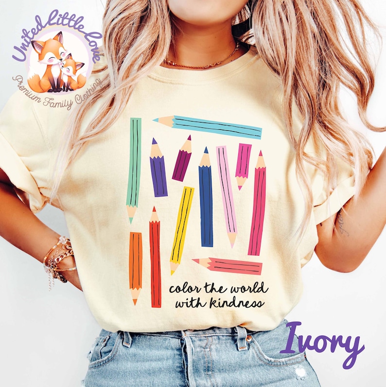 Peut inclure: T-shirt ivoire avec un motif de crayons color&eacute;s et le texte "color the world with kindness". Les crayons sont de diff&eacute;rentes couleurs, dont le vert, le violet, le jaune, le rose et l'orange. Le t-shirt a une coupe d&eacute;contract&eacute;e et des manches courtes.
