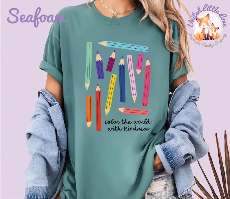 Peut inclure: T-shirt vert d'eau avec un motif de crayons color&eacute;s et le texte "color the world with kindness". Les crayons sont de diff&eacute;rentes couleurs, dont le bleu, le rose, le jaune et l'orange. Le t-shirt a des manches courtes et une coupe d&eacute;contract&eacute;e.