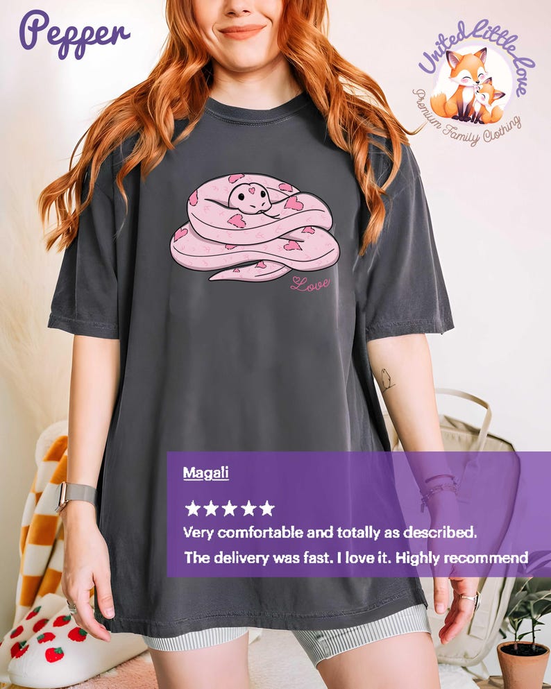 May include: Dark gray t-shirt featuring a pink snake design with heart accents and the word "Love". The shirt has short sleeves and a relaxed fit. The brand name "Pepper" is in the upper left corner.