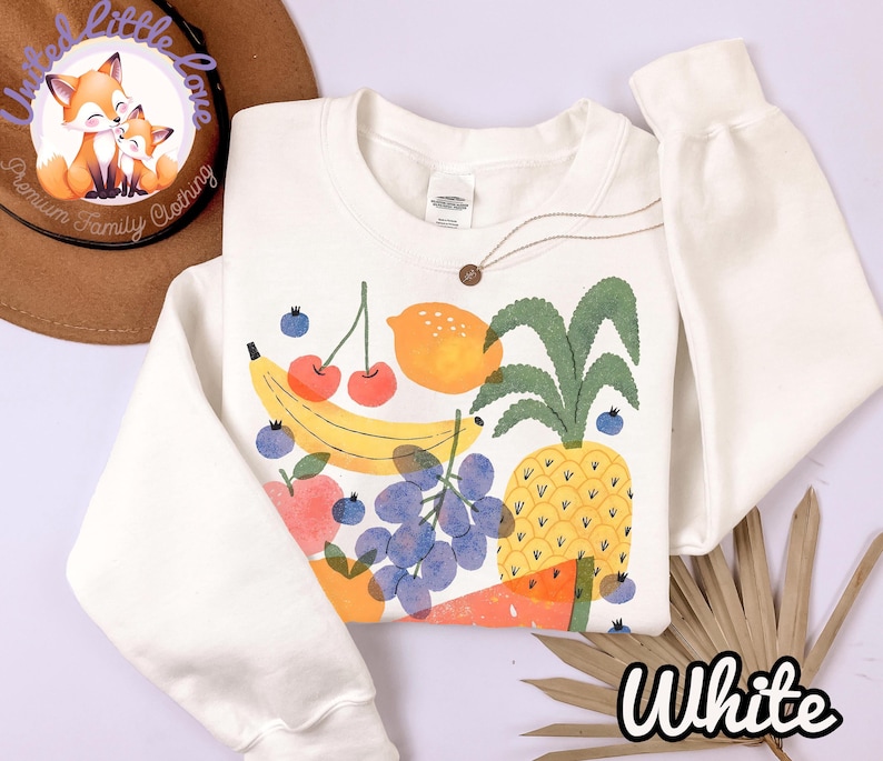 May include: White sweatshirt with a colorful fruit graphic including a banana, cherries, lemon, pineapple, grapes, and watermelon. The word "White" is written in a script font at the bottom right.