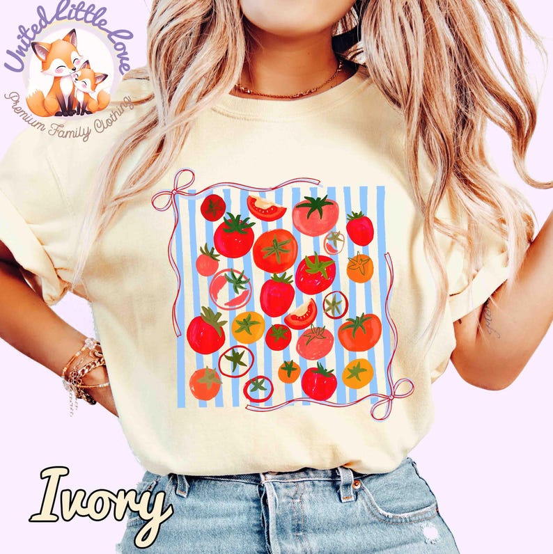 Peut inclure: T-shirt ivoire avec un motif de tomates sur un fond &agrave; rayures bleues et blanches. Le motif comprend des tomates rouges et oranges de diff&eacute;rentes tailles avec des feuilles vertes. Le t-shirt porte le texte "Ivory" en bas.