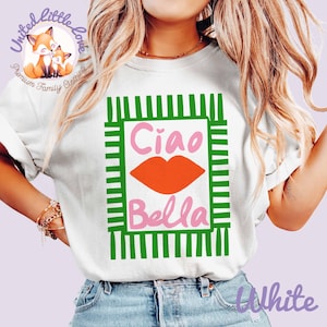 K&ouml;nnte beinhalten: Wei&szlig;es T-Shirt mit gr&uuml;n-wei&szlig;em Streifenbord&uuml;rendesign. Das Shirt zeigt die Worte "Ciao Bella" in Pink und eine orangefarbene Lippengrafik. Teil der Premium-Familienbekleidungslinie "United Little Love".