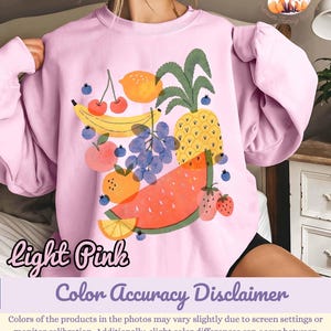 May include: Light pink sweatshirt featuring a colorful fruit graphic. The design includes a banana, cherries, grapes, orange, pineapple, watermelon, and strawberries. The words "light pink" are written in cursive on the bottom left.