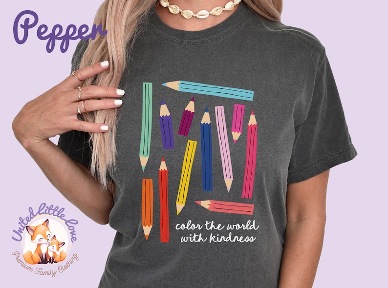 Peut inclure: T-shirt gris fonc&eacute; avec un motif de crayons color&eacute;s. Les crayons sont de diff&eacute;rentes couleurs, notamment bleu, vert, violet, jaune et rose. Le texte "color the world with kindness" est imprim&eacute; en dessous.
