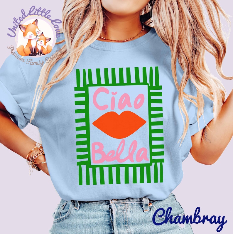 K&ouml;nnte beinhalten: Hellblaues T-Shirt mit einem gr&uuml;n-wei&szlig;en rechteckigen Design. Das Design zeigt die Worte "Ciao Bella" in Rosa, mit einer orangefarbenen Lippen-Grafik. Das Shirt hat kurze &Auml;rmel und ist aus einem weichen Material.