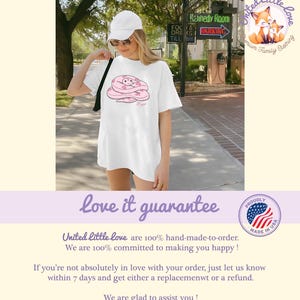 May include: White t-shirt featuring a pink cartoon snake design. The shirt is worn by a person wearing a white cap and sunglasses. The image includes text that reads "United little love" and "love it guarantee".