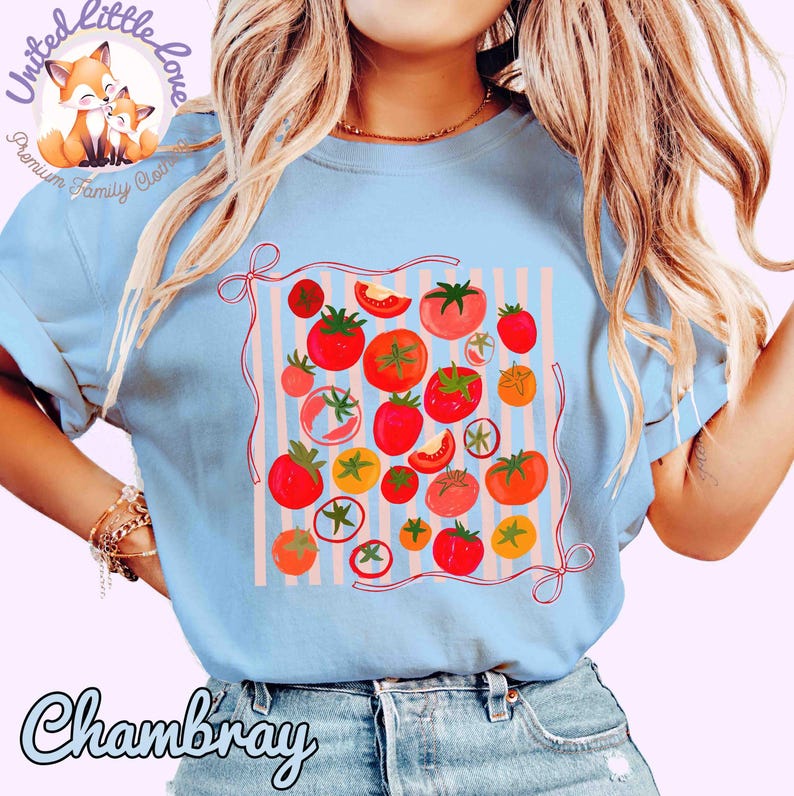 Peut inclure: T-shirt bleu clair avec un motif de tomates color&eacute;es. Le design pr&eacute;sente diverses tomates rouges, oranges et jaunes sur un fond ray&eacute;. Le mot "Chambray" est imprim&eacute; sur le t-shirt.