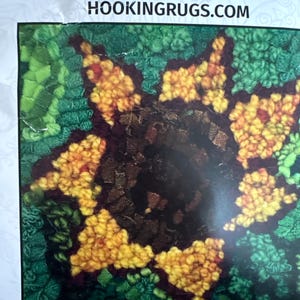 May include: A beginner rug hooking kit featuring a sunflower design. The sunflower has yellow petals and a dark brown center, set against a green background. The kit is approximately 6 x 6 inches and includes the text "BEGINNER SUNFLOWER".