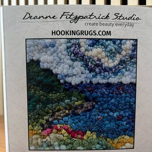 May include: A rug hooking kit titled "Sweet Bay" by Deanne Fitzpatrick Studio. The kit includes a 6" x 6" rug design with a colorful, textured pattern in shades of blue, green, pink, and yellow. The box also features the website HOOKINGRUGS.COM.