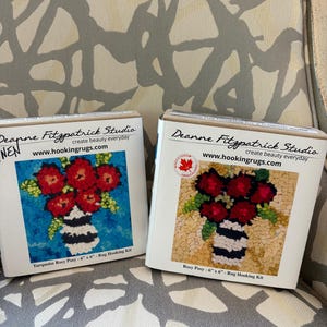 May include: Two rug hooking kits featuring floral designs. One kit has a turquoise background, the other a beige background. Both kits display a vase with red flowers and the text "Deanne Fitzpatrick Studio" and "www.hookingrugs.com". Each kit is 6" x 6".