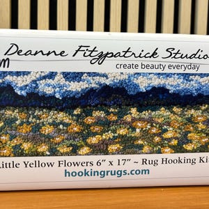 May include: A rug hooking kit titled "Little Yellow Flowers" by Deanne Fitzpatrick Studio. The kit features a colorful design of yellow flowers, blue sky, and green foliage. The dimensions are 6" x 17". The text "create beauty everyday" is also visible.