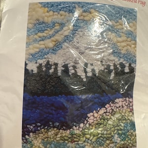 May include: A rug hooking kit with the text "RUG HOOKING KIT" and "Get ready to create your own beautiful hooked rug." The kit features a colorful design of a mountain landscape. The finished rug size is 7" x 9".