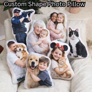 May include: Custom shape photo pillows featuring various images, including a police officer, children, a baby with a grandmother, a cat, a dog, and a boy with a dog. The pillows are on a white surface. The text "Custom Shape Photo Pillow" is at the top.