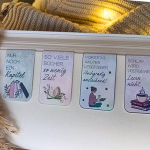 Könnte beinhalten: Vier rechteckige Lesezeichen mit Pastellhintergründen und Text. Die Lesezeichen zeigen Illustrationen von Büchern, einer lesenden Person und einer Tasse Kaffee. Der Text enthält Sätze wie "Nur noch ein Kapitel" und "So viele Bücher, so wenig Zeit."