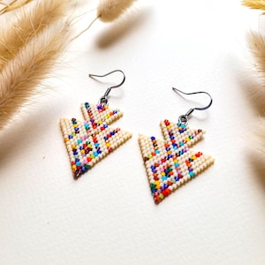 Peut inclure: Une paire de boucles d'oreilles en perles de couleur crème en forme triangulaire. Les boucles d'oreilles sont décorées de perles colorées dans une variété de couleurs, dont le rouge, le bleu, le vert et le jaune. Les boucles d'oreilles ont des crochets argentés.
