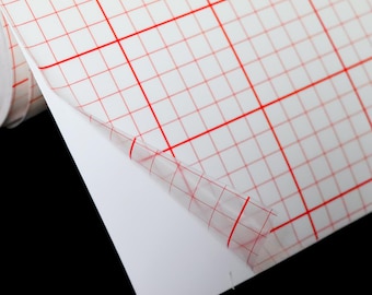 May include: A roll of clear adhesive-backed grid paper with red lines. The paper is partially unrolled, revealing the adhesive backing.