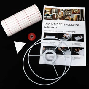 May include: A white lampshade frame with instructions on how to create a lampshade using fabric. The instructions are in Italian and include a gridded fabric, a red spool of thread, and a white triangle.
