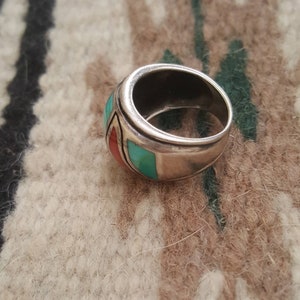 May include: A silver ring with turquoise and red stones set in a wide band.