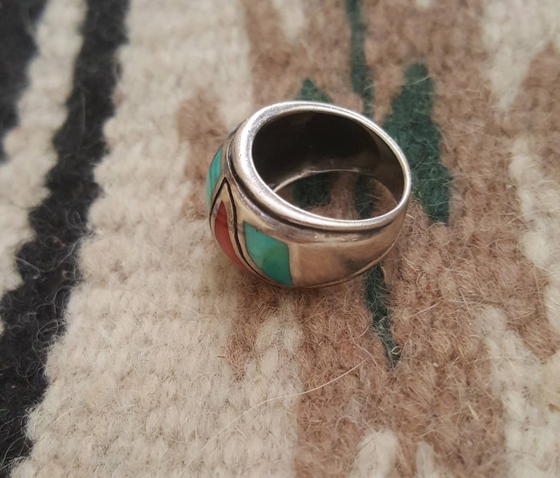 May include: A silver ring with turquoise and red stones set in a wide band.