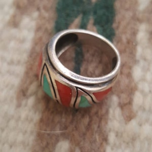 May include: A silver ring with a wide band featuring a geometric design inlaid with turquoise and coral stones.
