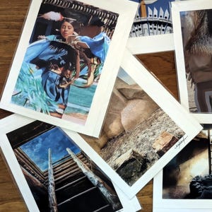 May include: A collection of framed art prints featuring Native American themes. The prints showcase images of a Native American dancer in a blue dress, a ladder leading to the sky, and architectural details. The prints are matted in white.