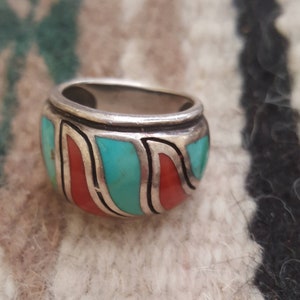 May include: A silver ring with turquoise and coral inlay. The ring is wide and has a rounded shape. The turquoise and coral are set in a silver band.