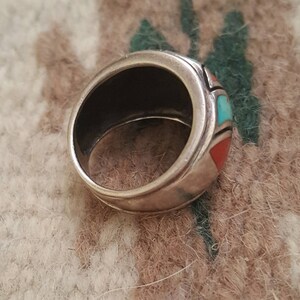 May include: A silver ring with turquoise and coral inlay. The ring is set in a wide band with a smooth, polished finish.