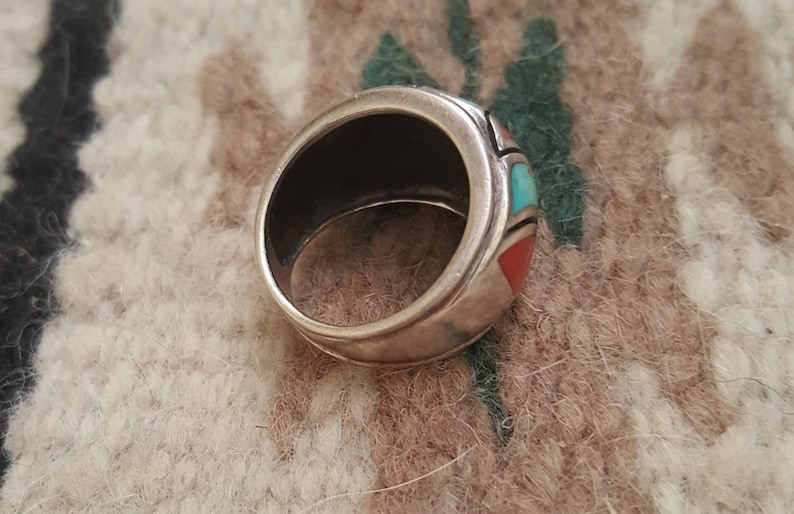 May include: A silver ring with turquoise and coral inlay. The ring is set in a wide band with a smooth, polished finish.
