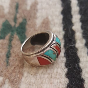 May include: A silver ring with turquoise and red stones set in a geometric pattern.