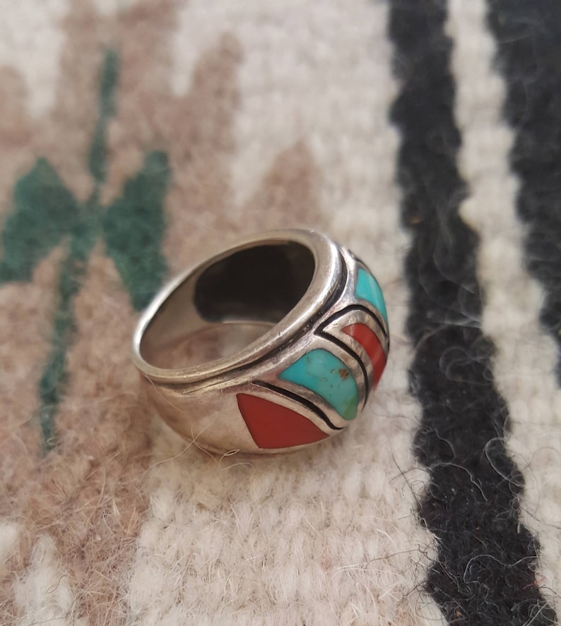 May include: A silver ring with turquoise and red stones set in a geometric pattern.