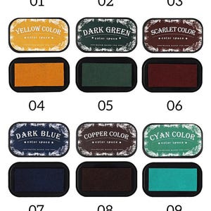 May include: A collection of 12 ink pads in various colors, including black, gold, red, yellow, dark green, scarlet, dark blue, copper, cyan, gray, blue, and purple. Each pad is labeled with its color and a number.