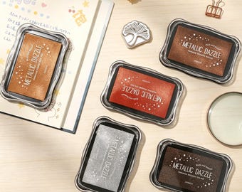 Metallic Pigment Ink Pad, available in gold, silver, black, red, copper, and brown, suitable for journals, scrapbooks, and crafts.