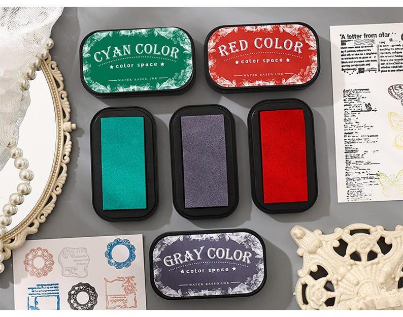 May include: A collection of ink pads in cyan, red, and gray, each labeled with its color name. The pads are rectangular with rounded corners and black bases. The text "color space" is also visible on the labels. The image also includes decorative elements.