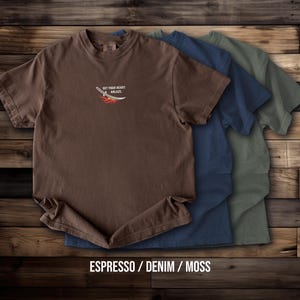 Puede incluir: Tres camisetas de manga corta y cuello redondo en colores espresso, denim y musgo. La parte frontal de la camiseta espresso presenta un peque&ntilde;o gr&aacute;fico de una espada con llamas y el texto "SET YOUR HEART ABLAZE" impreso en color blanco.