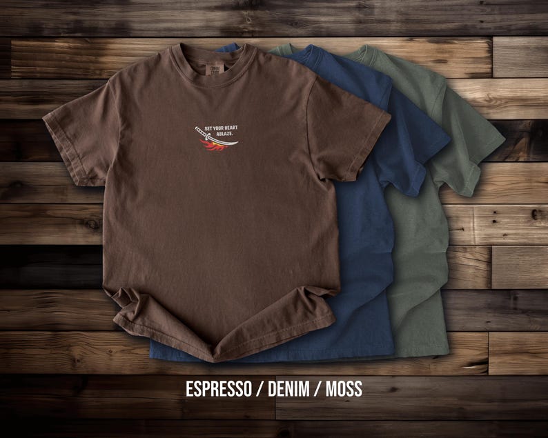 Puede incluir: Tres camisetas de manga corta y cuello redondo en colores espresso, denim y musgo. La parte frontal de la camiseta espresso presenta un peque&ntilde;o gr&aacute;fico de una espada con llamas y el texto "SET YOUR HEART ABLAZE" impreso en color blanco.