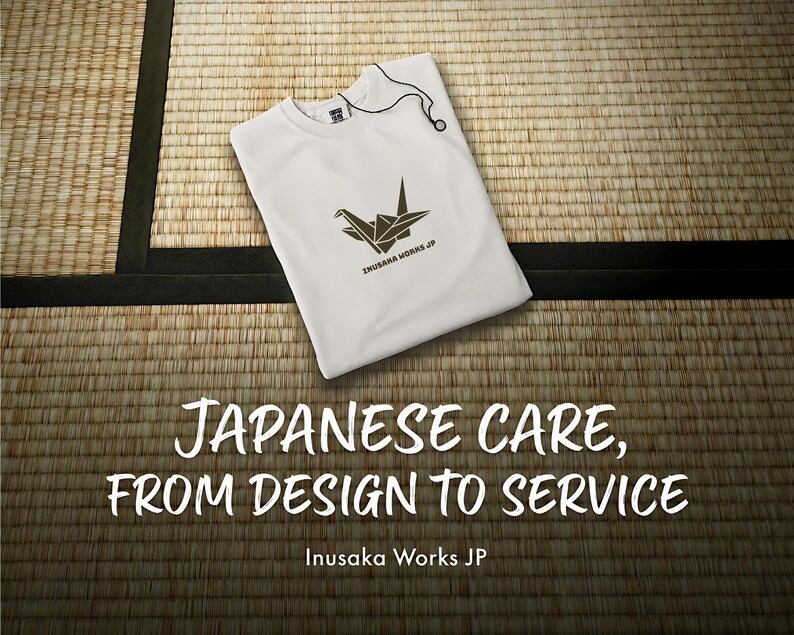 Puede incluir: Una camiseta blanca con un gr&aacute;fico marr&oacute;n oscuro de una grulla de origami y el texto Inusaka Works JP. La prenda incluye una etiqueta con cord&oacute;n negro en el cuello. El texto Japanese care, from design to service aparece debajo.