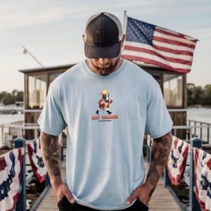 May include: Light blue t-shirt featuring a cartoon bulldog wearing a yellow hat and red jacket, walking with a cane. The text "Keep Walking" is below the graphic. A black and gray trucker hat is worn.