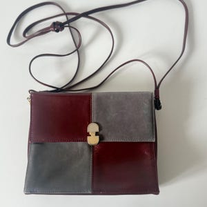 May include: A burgundy and gray leather crossbody bag with a long, thin strap. The bag is divided into four sections, two burgundy and two gray, with a gold-colored clasp.