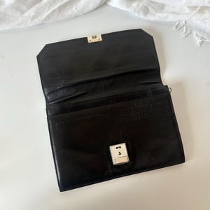 May include: Black leather wallet with a silver clasp. The wallet is open, showing several card slots. The rectangular wallet has a shiny finish and a classic design. The background is white.
