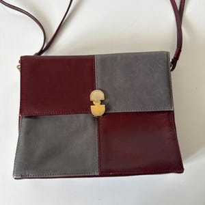 May include: A burgundy and gray leather crossbody bag with a gold-tone clasp. The bag is divided into four sections, two burgundy and two gray, with a long burgundy strap.
