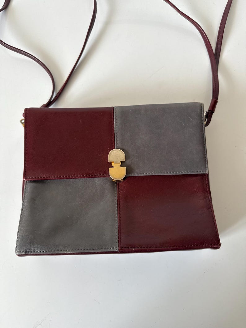 May include: A burgundy and gray leather crossbody bag with a gold-tone clasp. The bag is divided into four sections, two burgundy and two gray, with a long burgundy strap.