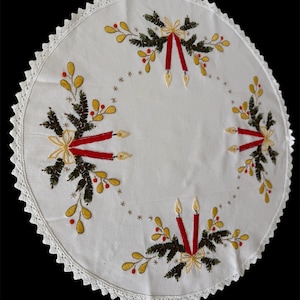 May include: White circular tablecloth with embroidered Christmas candle and evergreen designs. Features red candles, yellow berries, and a scalloped lace edge. A festive holiday table decoration.