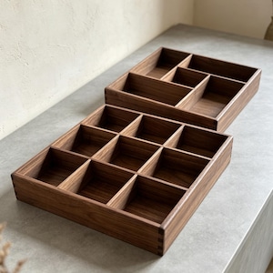 May include: Two rectangular wooden organizer trays crafted from dark brown wood with visible grain. One tray features a nine-compartment grid, while the other contains five varied sections. Both trays have box-joint corners and open tops.