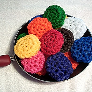 May include: A collection of colorful crocheted pot scrubbers in a black frying pan. The scrubbers are in various colors, including red, blue, green, yellow, orange, and white.