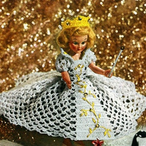 May include: A white crocheted doll dress with a yellow crown and a gold vine design. The doll is holding a wand.